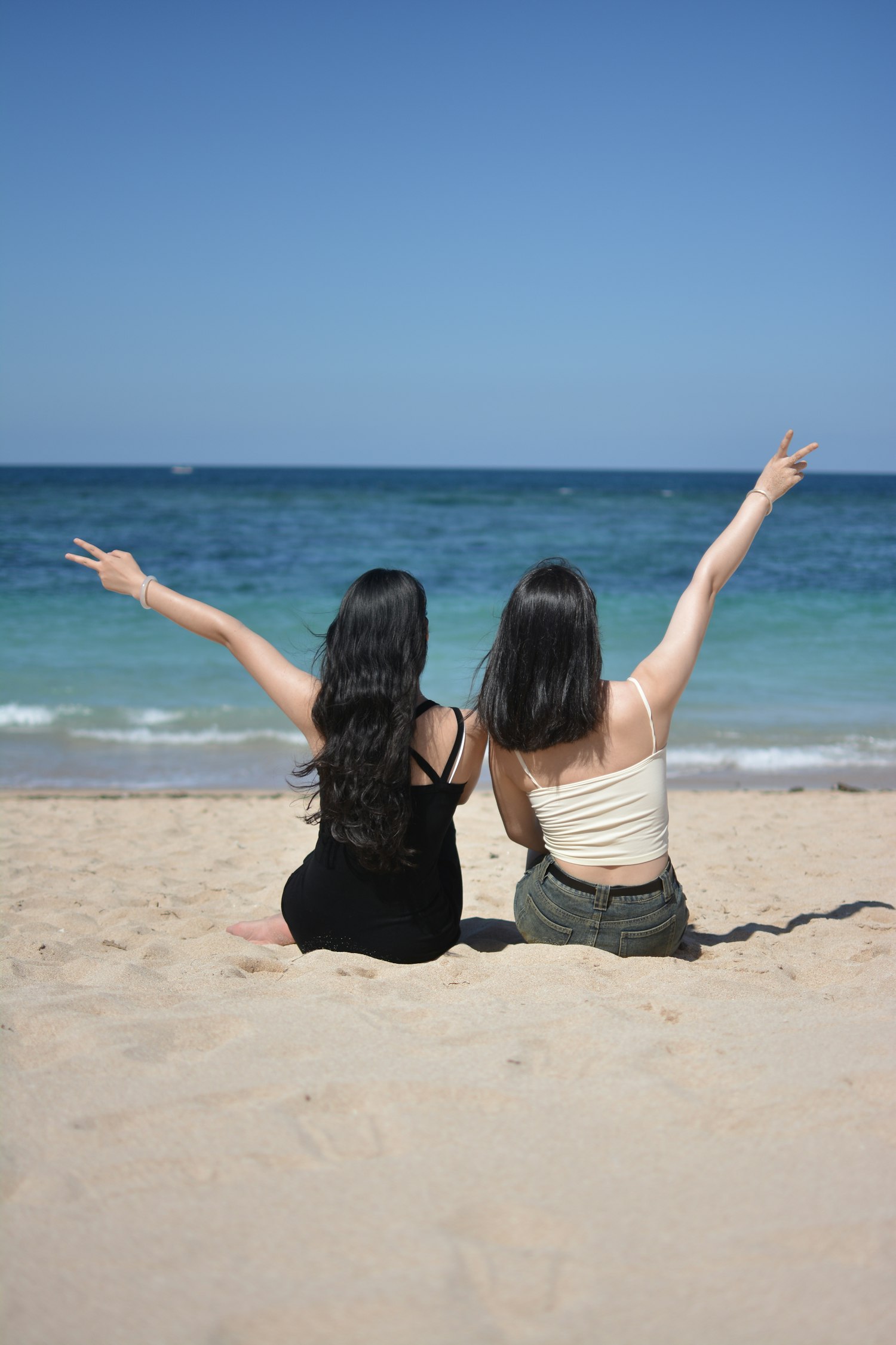 Deux amis bras levés sur la plage, pleins de joie.
